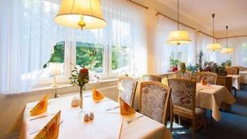 A dining area with tables set for a meal, featuring a view of greenery outside.