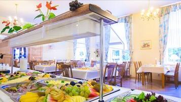 A buffet with various fruits and vegetables, wooden chairs, and tables with white tablecloths.
