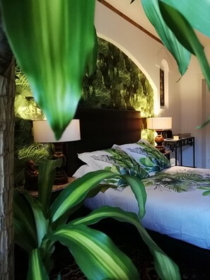 Ein Schlafzimmer mit einem Bett, zwei Nachttischen, einer Stehlampe und einer großen Kübelpflanze.