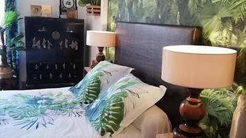 A bedroom with a bed, two bedside lamps, a dark wooden headboard, a wall mural, a dark wooden dresser, and a small plant.
