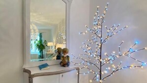 A white console table with a mirror, a small plant, and a decorative tree with lights. - Clos Germanois (Saint-Germain-Laval)