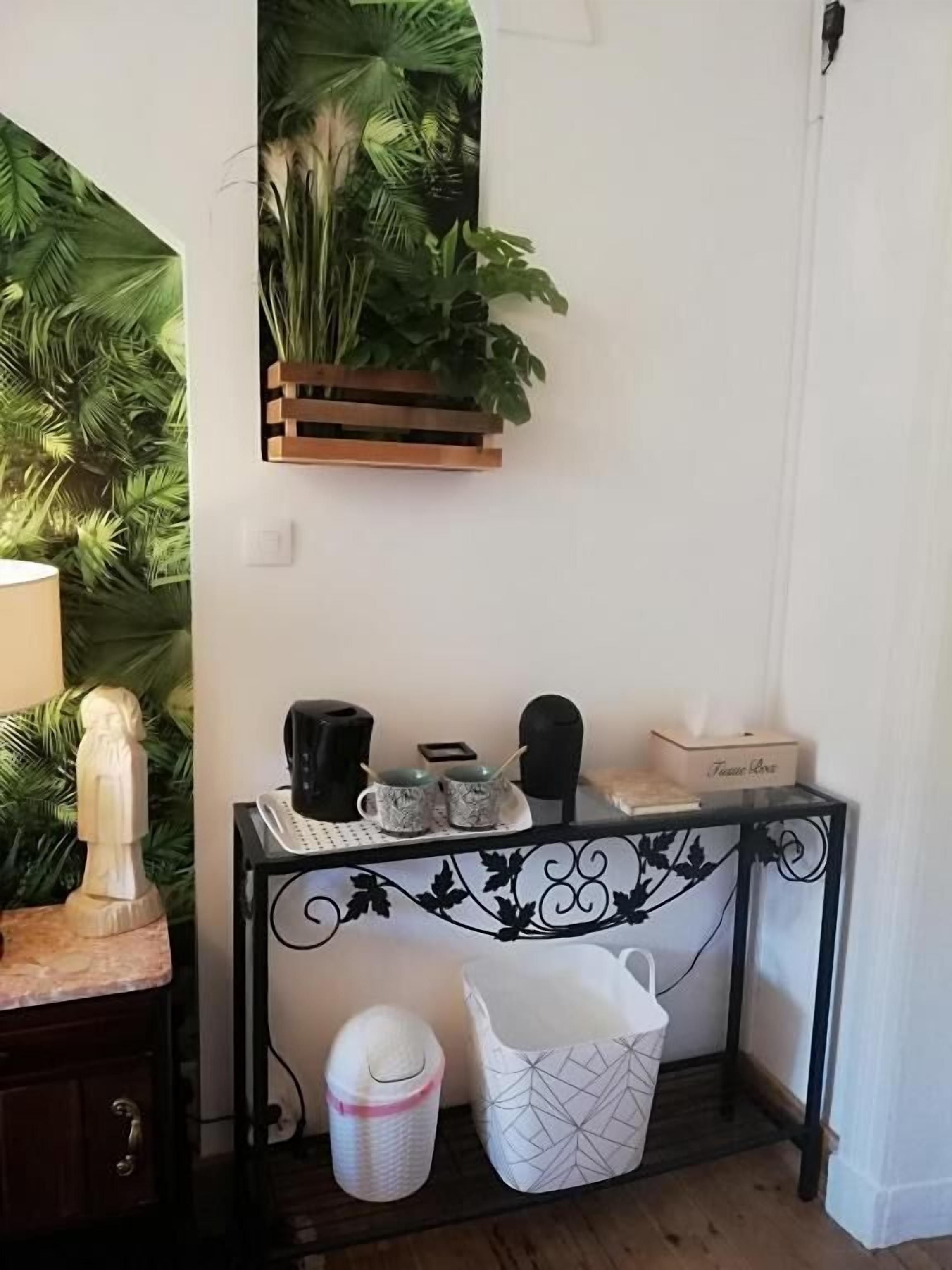A corner of a room with a wooden console table, a white basket, a black trash bin, and a wall-mounted plant shelf.