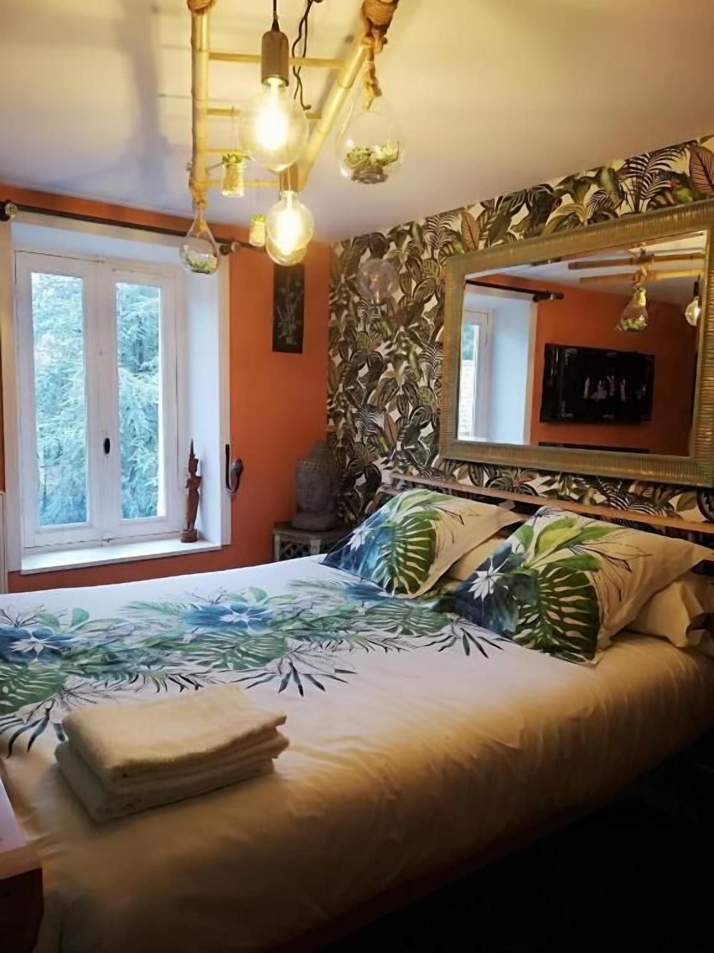 Un dormitorio con cama, ventana, espejo y pared con diseño de hojas tropicales.