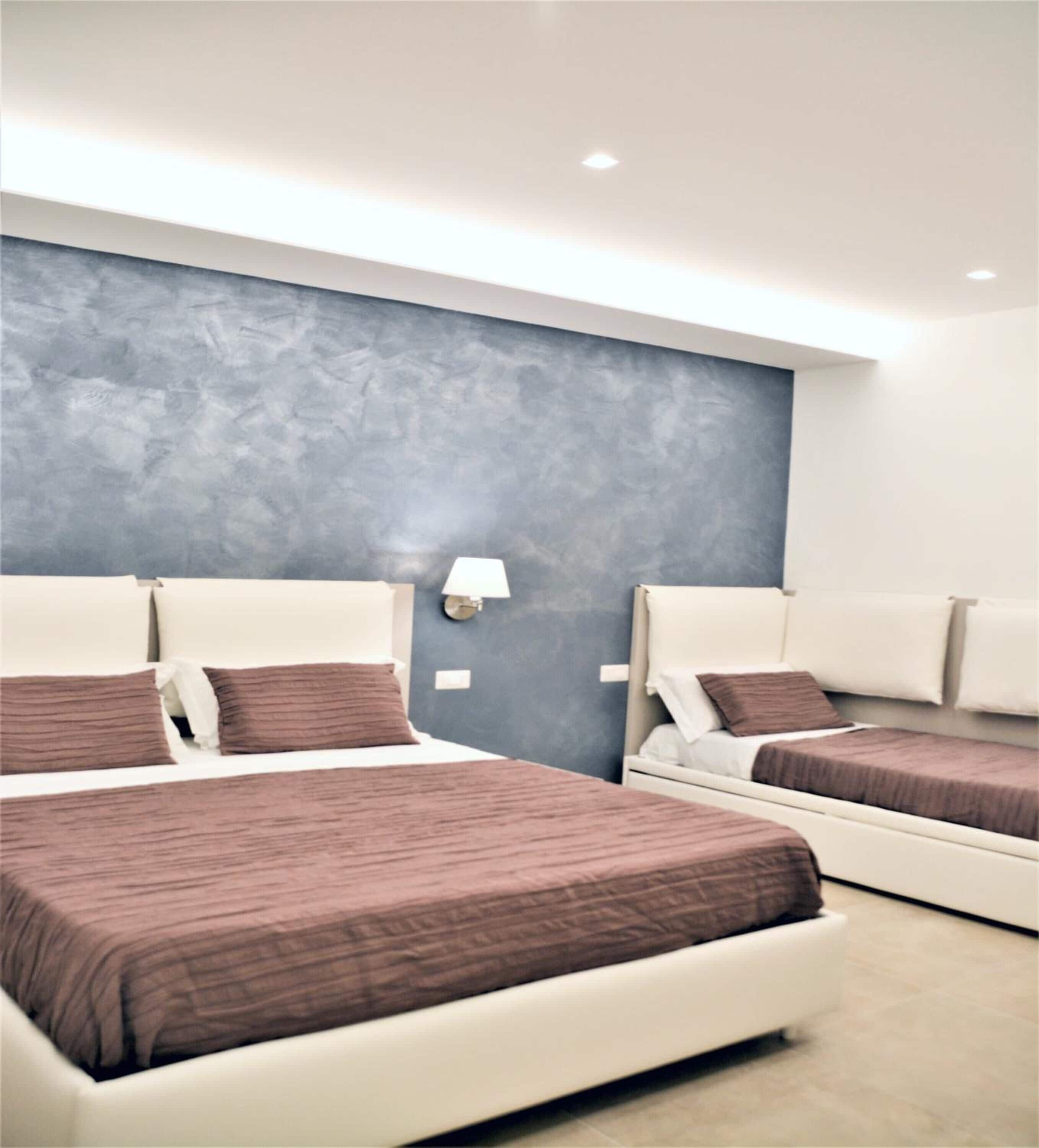 A modern hotel room with two beds, a grey textured wall, and a white ceiling.