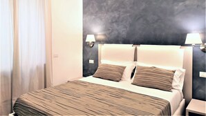 Et hotelværelse med en seng, to sengeborde med lamper, en mørk væg med struktur og et vindue med gardiner.