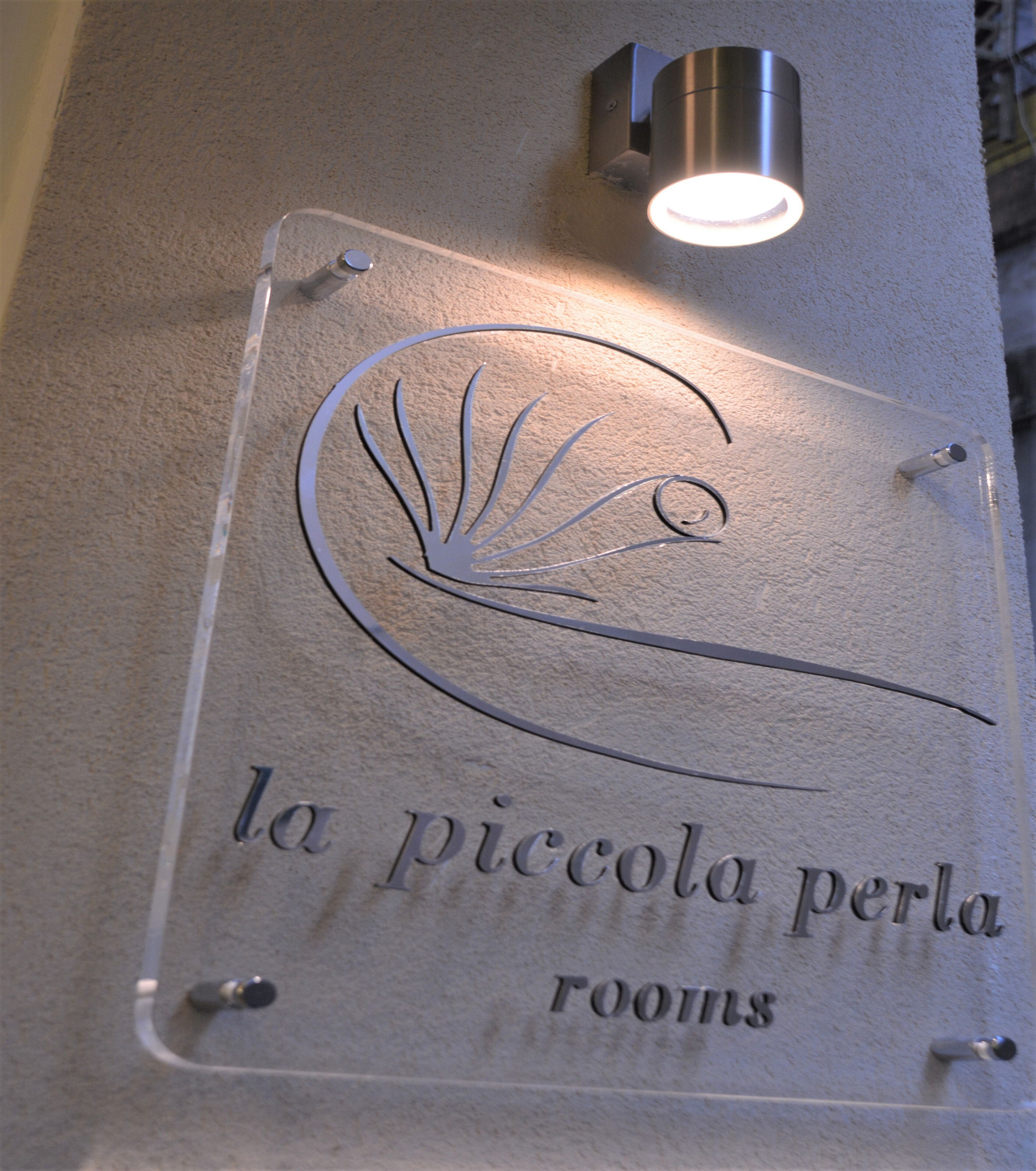 A clear sign with a shell design and the text "la piccola perla rooms".