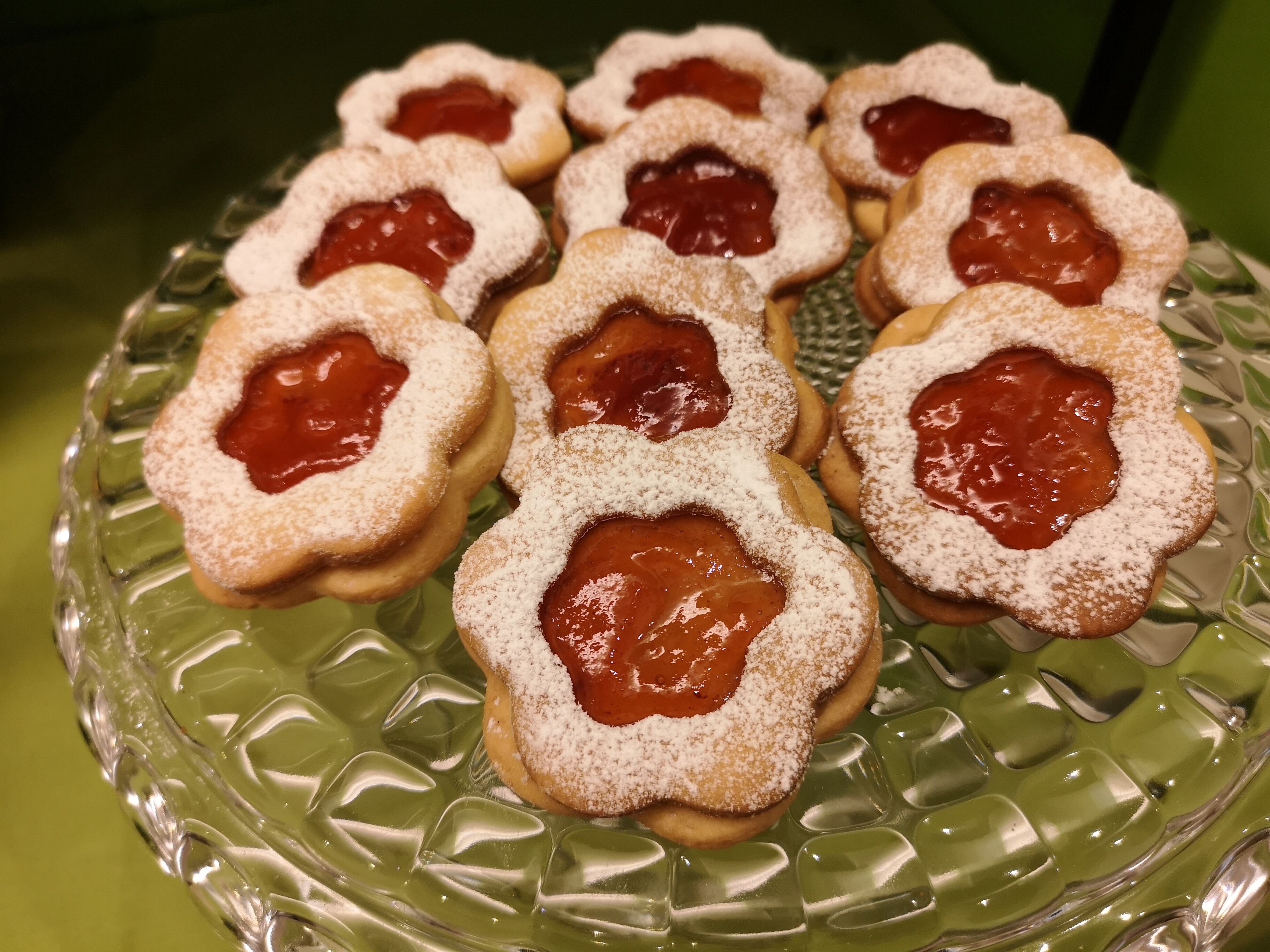 A green glass plate with round cookies topped with powdered sugar and jam.