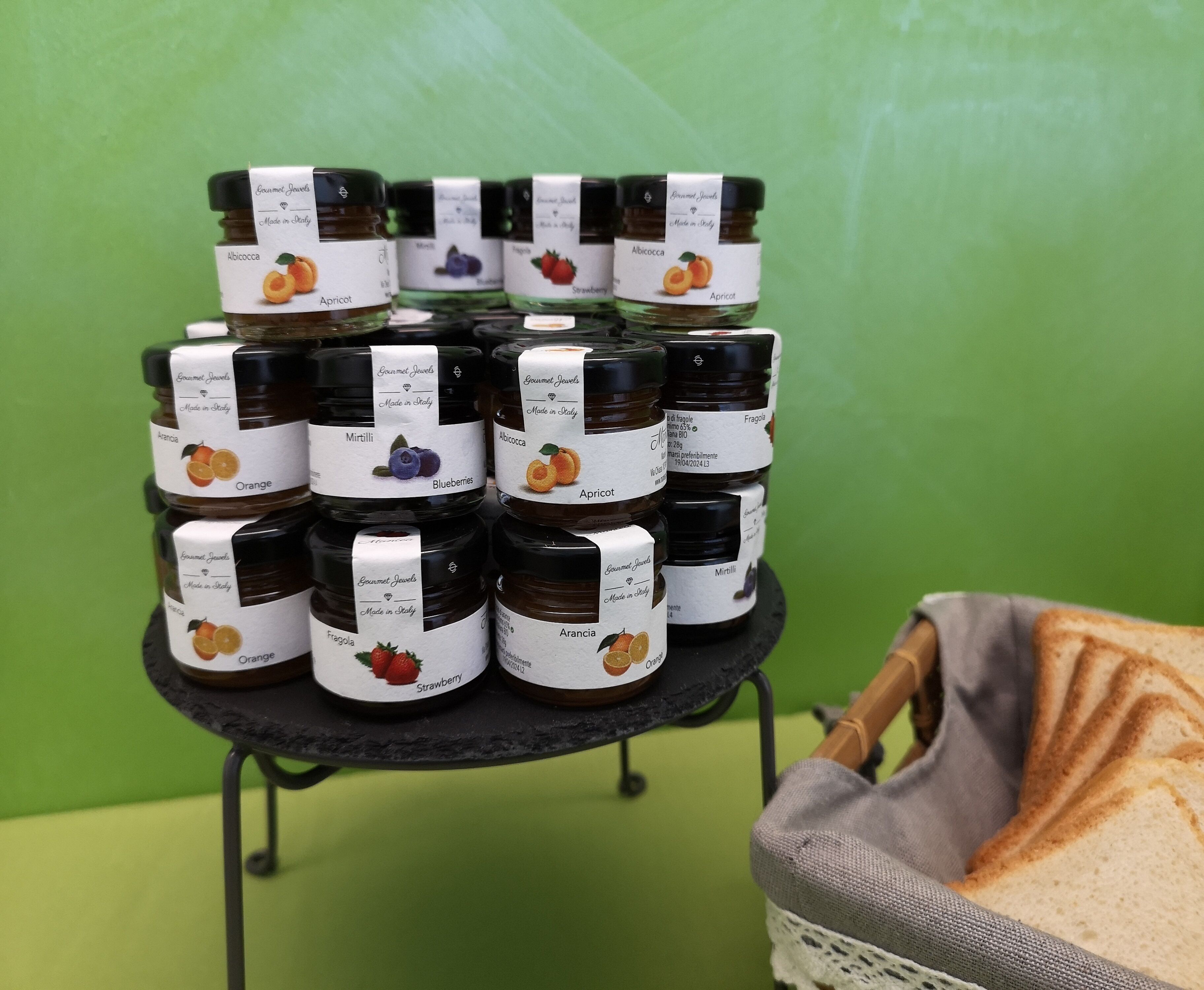 A display of various flavored honey jars on a black stand against a green background.