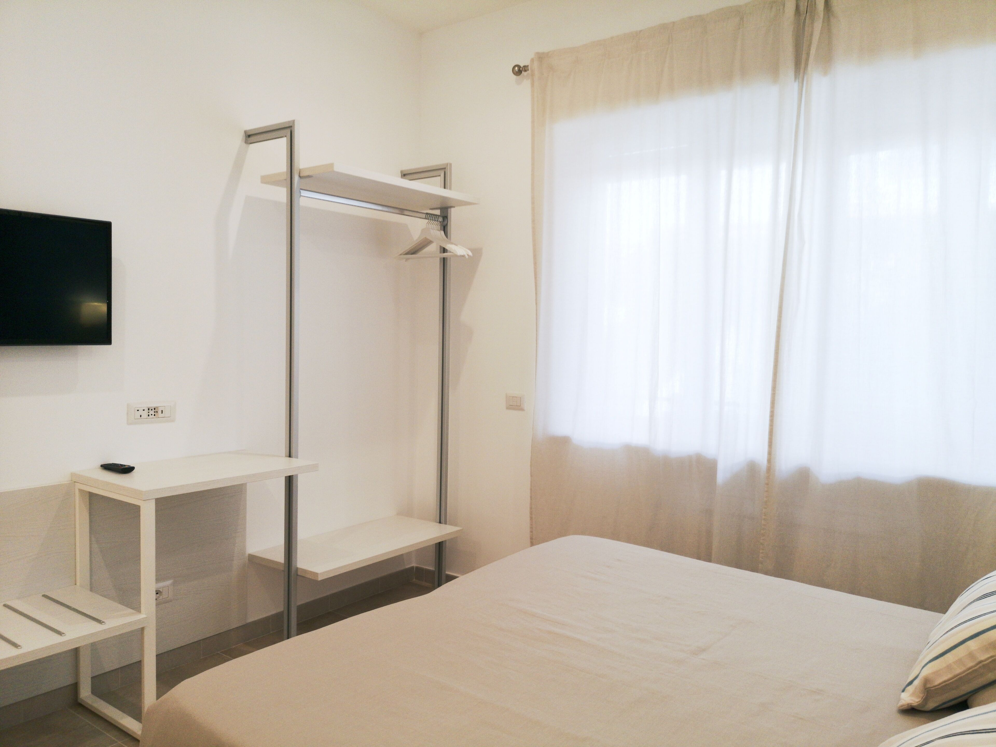 Une chambre à coucher avec un lit, un téléviseur fixé au mur, une armoire et une fenêtre avec des rideaux.