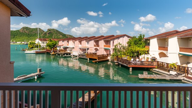 A waterfront hotel with multiple buildings, docked boats, and a clear view of the water and mountains in the background.