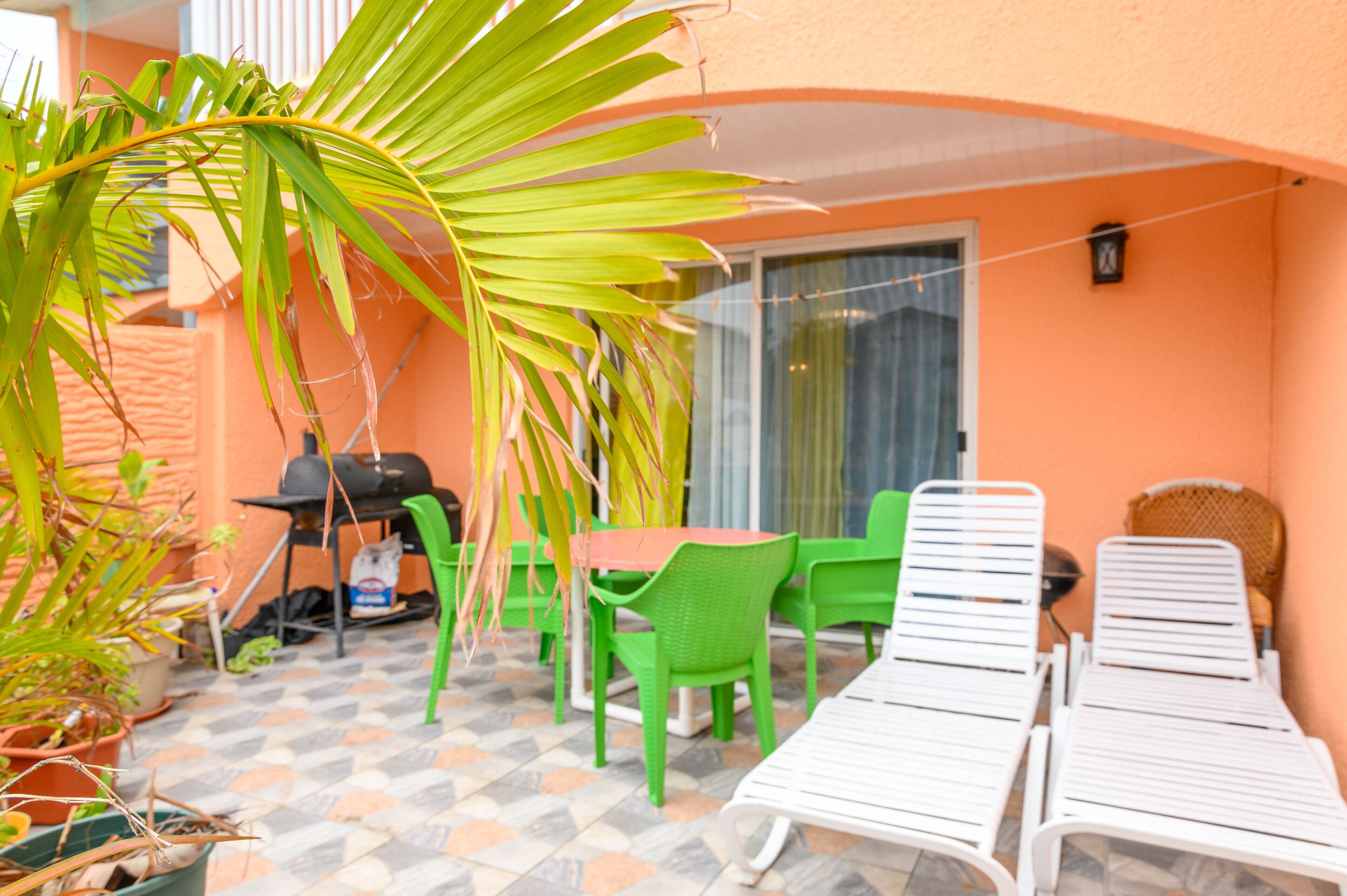 Eine Terrasse mit Tisch, Stühlen, einem Grill und einer Palme.