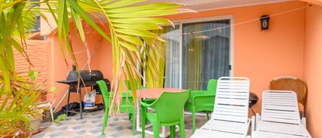 Eine Terrasse mit Tisch, Stühlen, einem Grill und einer Palme.