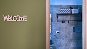 Une salle de bain avec un mur recouvert de carreaux gris, un porte-serviettes et une étagère sur laquelle reposent un coussin à motifs et un panier.