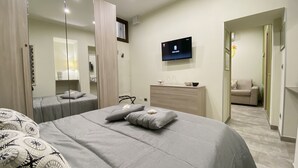 Une chambre d’hôtel moderne avec deux lits, une télévision, une commode et un canapé dans la pièce adjacente.