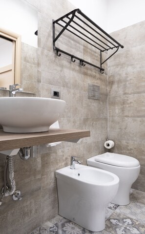 Ein modernes Badezimmer mit einem großen Waschbecken, zwei Toiletten und einem Handtuchhalter.