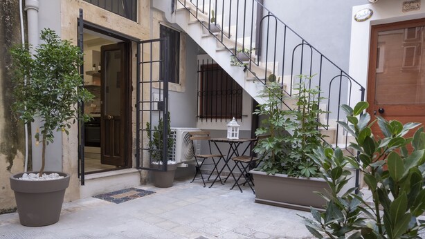 Une cour intérieure avec un escalier, des plantes en pot et une petite table entourée de chaises.
