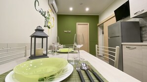 Un coin repas avec une table dressée pour deux personnes, un tapis vert, une lanterne et une pancarte « Bienvenue » accrochée au mur.