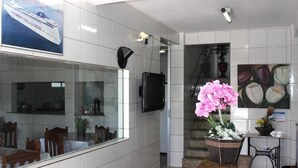 A hotel lobby with a large window, a flat-screen TV mounted on the wall, and a potted pink orchid on a brown rug. - Hotel Rey (Camaçari)