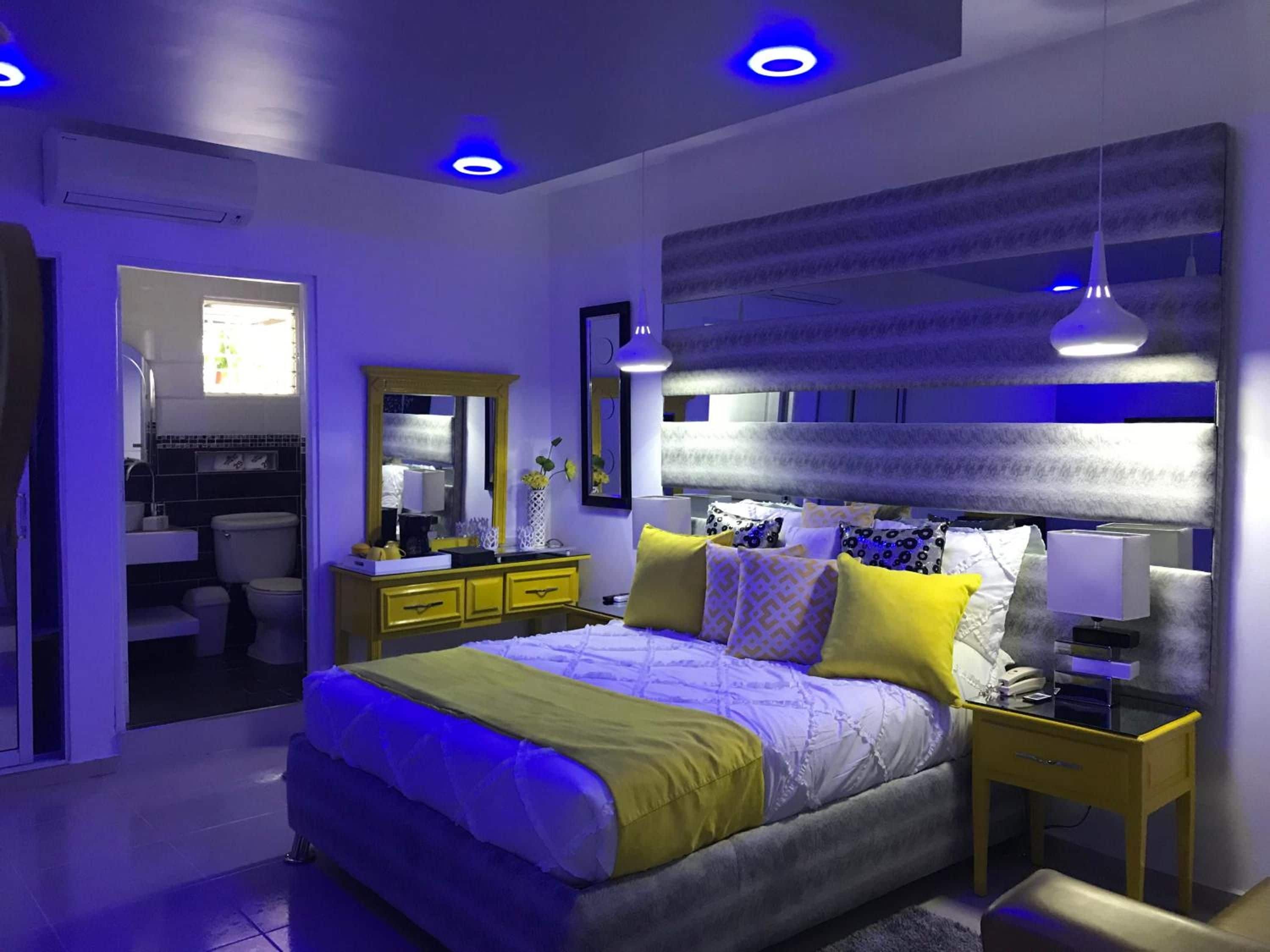 Ein modernes Schlafzimmer mit Bett, Nachttischen, einem Spiegel und einem durchgegangenen Tür sichtbaren Badezimmer.