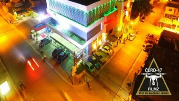 A modern building with a flat roof and a large glass facade, surrounded by parked cars and a street at night. - Hotel Rey (Camaçari)