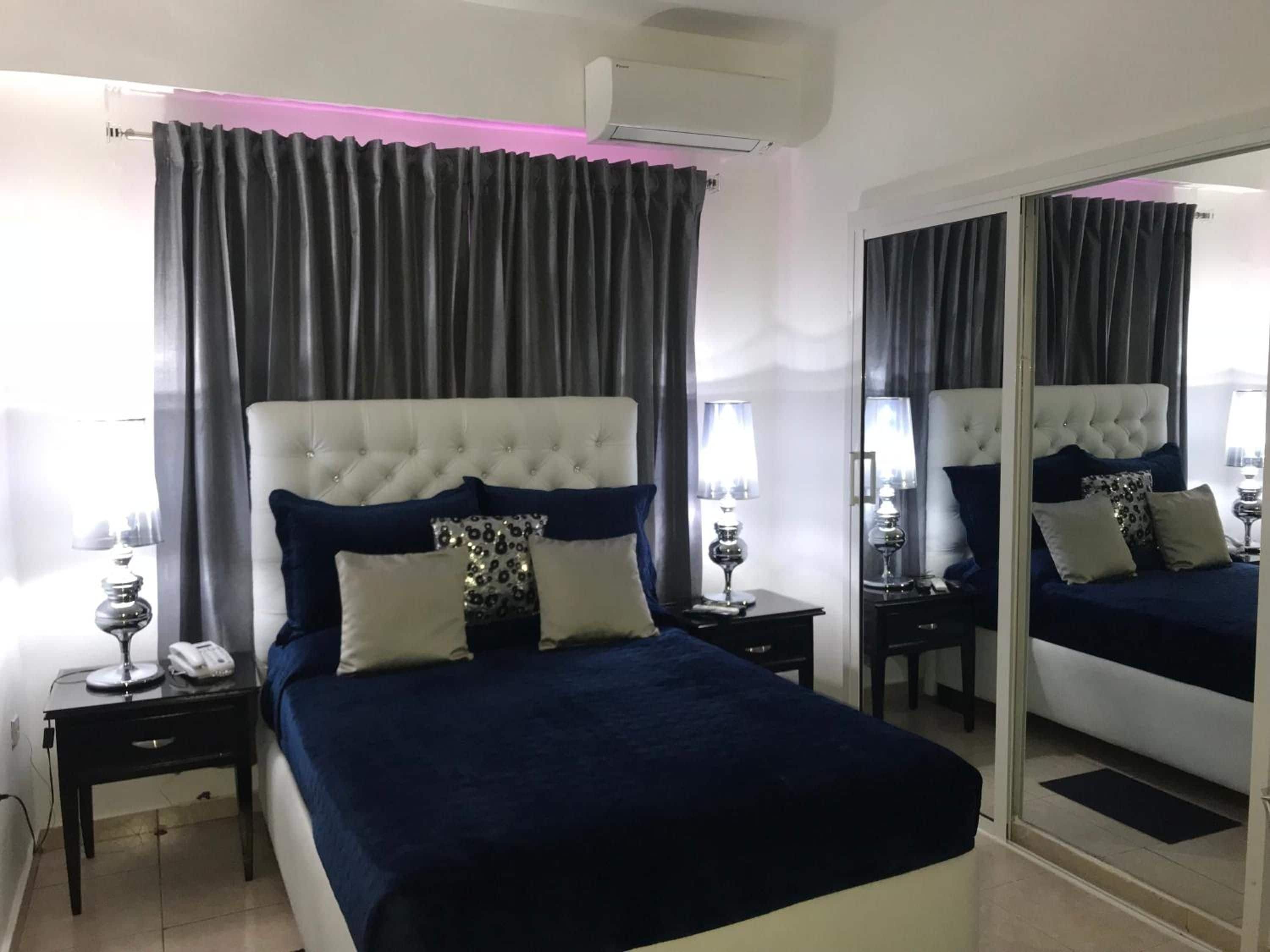 Une chambre à coucher avec un grand lit, une table de chevet avec une lampe, un miroir et une fenêtre avec des rideaux.
