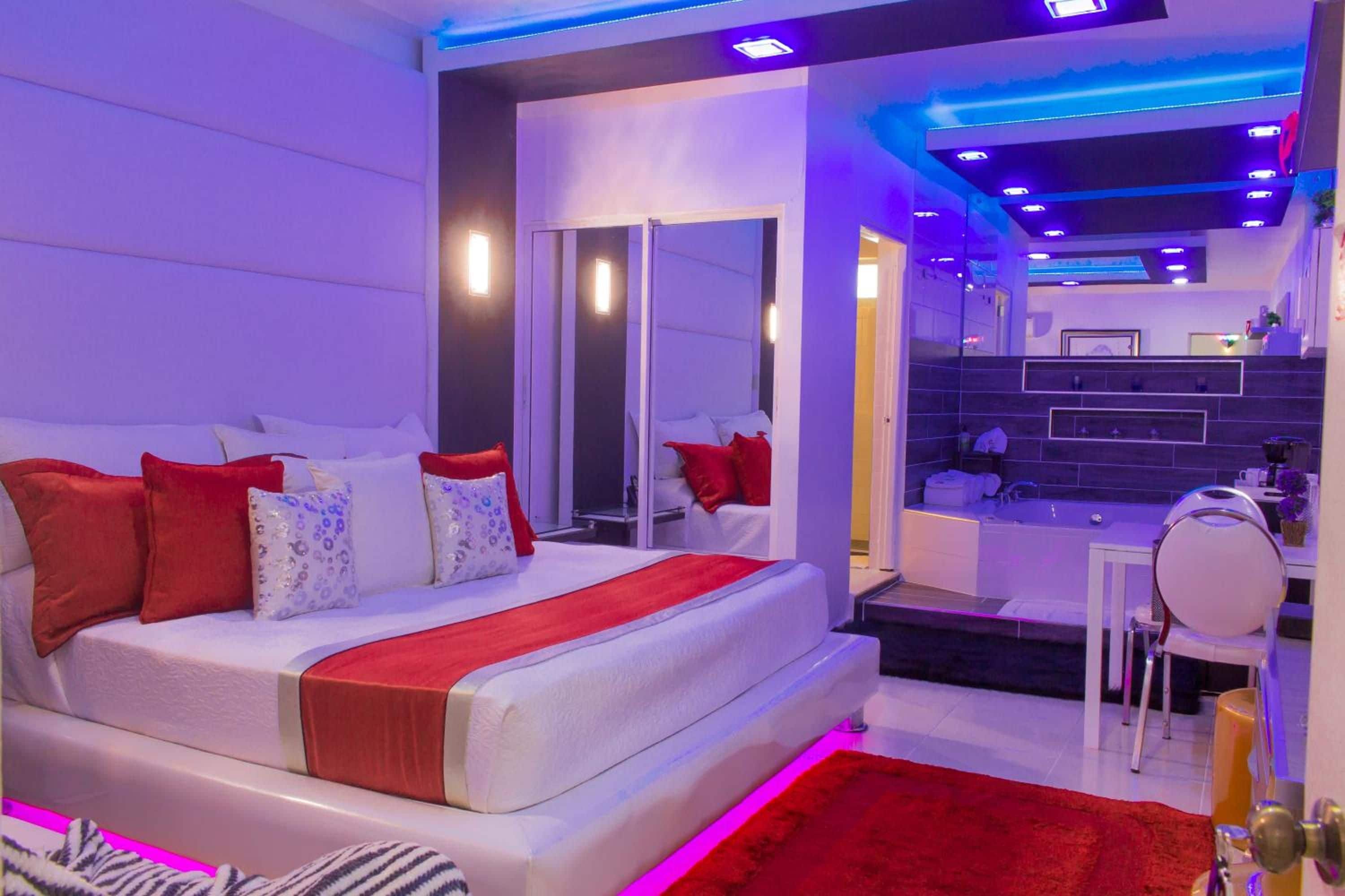 A modern bedroom with a large bed, a bathroom with a bathtub, and a kitchenette.