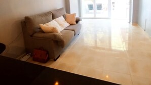 Un salon moderne avec un canapé, un sac rouge et un couloir menant à une porte en verre.