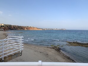 A coastal beach with a white metal railing in the foreground, a sandy shore, and a rocky outcrop with buildings in the background. - Casa Maria 800 meters from the beach with restaurants  (Campoamor)