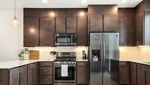 A modern kitchen with dark wood cabinets, stainless steel appliances, and a white countertop.