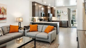 A modern living room with a grey sofa and orange cushions, a coffee table, and a painting on the wall.
