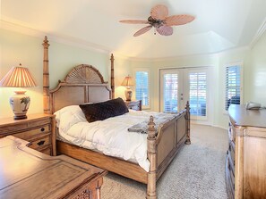 A bedroom with a wooden bed, a ceiling fan, and a view of the outside through the door.