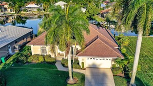 A residential area with a house featuring a red roof, surrounded by well-maintained lawns and palm trees. - Marco Island Pool Home with Water View and Direct Access to the Gulf (Marco Island)