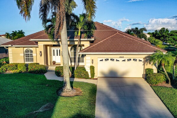 A residential house with a garage, a well-maintained lawn, and palm trees.