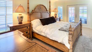 A bedroom with a wooden bed, two bedside tables, a ceiling fan, and a view through the window. - Marco Island Pool Home with Water View and Direct Access to the Gulf (Marco Island)