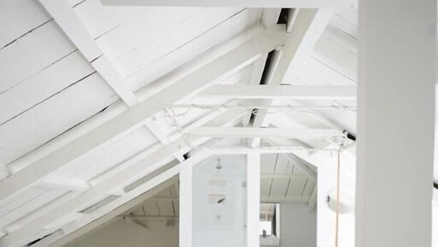 Quarto moderno com decoração em branco, teto inclinado, cama com roupa de cama branca e tapete listrado em preto e branco.