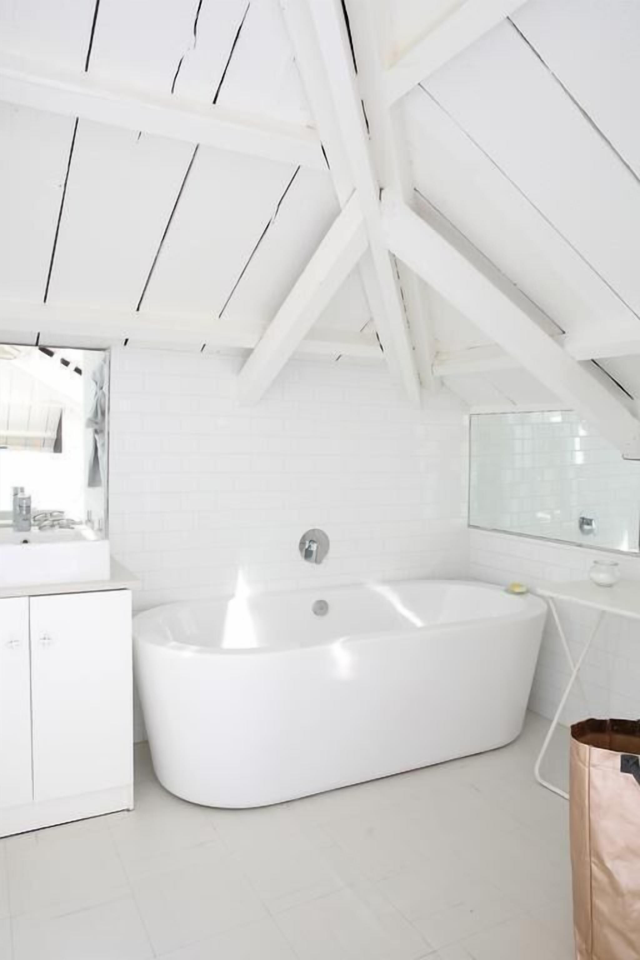 A modern bathroom with a freestanding bathtub, a large mirror, and white cabinetry.