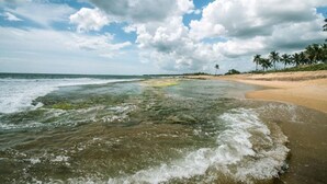 A beach with clear water, sandy shore, and palm trees under a partly cloudy sky. - Ladja Beach Resort (Ambalantota)