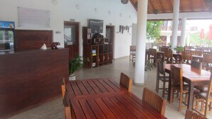 A restaurant with wooden furniture, a reception desk, and a TV. - Ladja Beach Resort (Ambalantota)