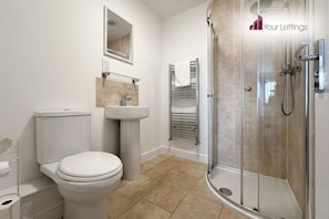 A bathroom with a toilet, sink, mirror, towel rack, and a glass-enclosed shower.