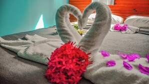 A bed with a heart-shaped towel arrangement, a red decorative item, and scattered purple flowers. - Pousada Casa Nui by Concavus (Ipojuca)