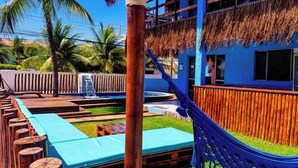 A pool area with wooden loungers, a hammock, and a thatched roof structure. - Pousada Casa Nui by Concavus (Ipojuca)