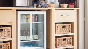 A compact kitchenette with a coffee maker, a mini-fridge stocked with beverages, and wicker baskets.