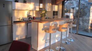 A modern kitchen with a central island, bar stools, and a view of the outside. - Chambres d'hotes La Petite Charnasserie (Angers)