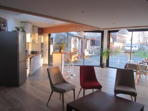 Amplia sala de estar con cocina, mesa y sillas para comer. Un gran ventanal ofrece vistas al exterior.