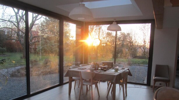 A dining area with a table set for four, large windows, and a view of the outdoors. - Chambres d'hotes La Petite Charnasserie (Angers)