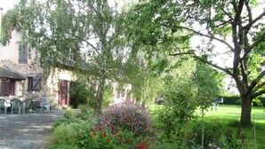 A stone building with a gravel path and a garden with various plants and flowers. - Chambres d'hotes La Petite Charnasserie (Angers)