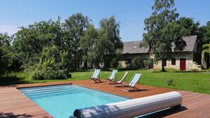 A rectangular swimming pool with a wooden deck, three striped lounge chairs, and a white floating lounge chair. - Chambres d'hotes La Petite Charnasserie (Angers)