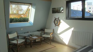 A room with a sloped ceiling, a view of the outside, a wooden table, two chairs, and a ship's wheel decoration. - Chambres d'hotes La Petite Charnasserie (Angers)
