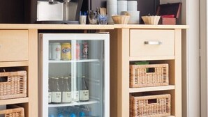 Een compacte kitchenette met een koffieapparaat, een minibar gevuld met drankjes, rieten manden en een klein kastje.
