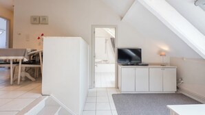 Une pièce moderne et bien éclairée, comprenant un coin repas, un téléviseur posé sur un meuble et un escalier menant à un autre niveau.